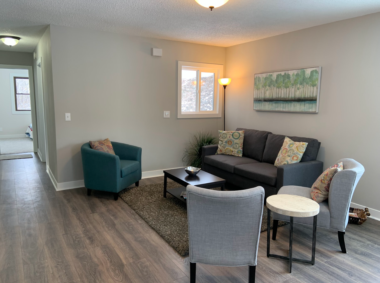 Living room with gray walls, sofa, teal chair, rug, coffee table, art, and hallway view.