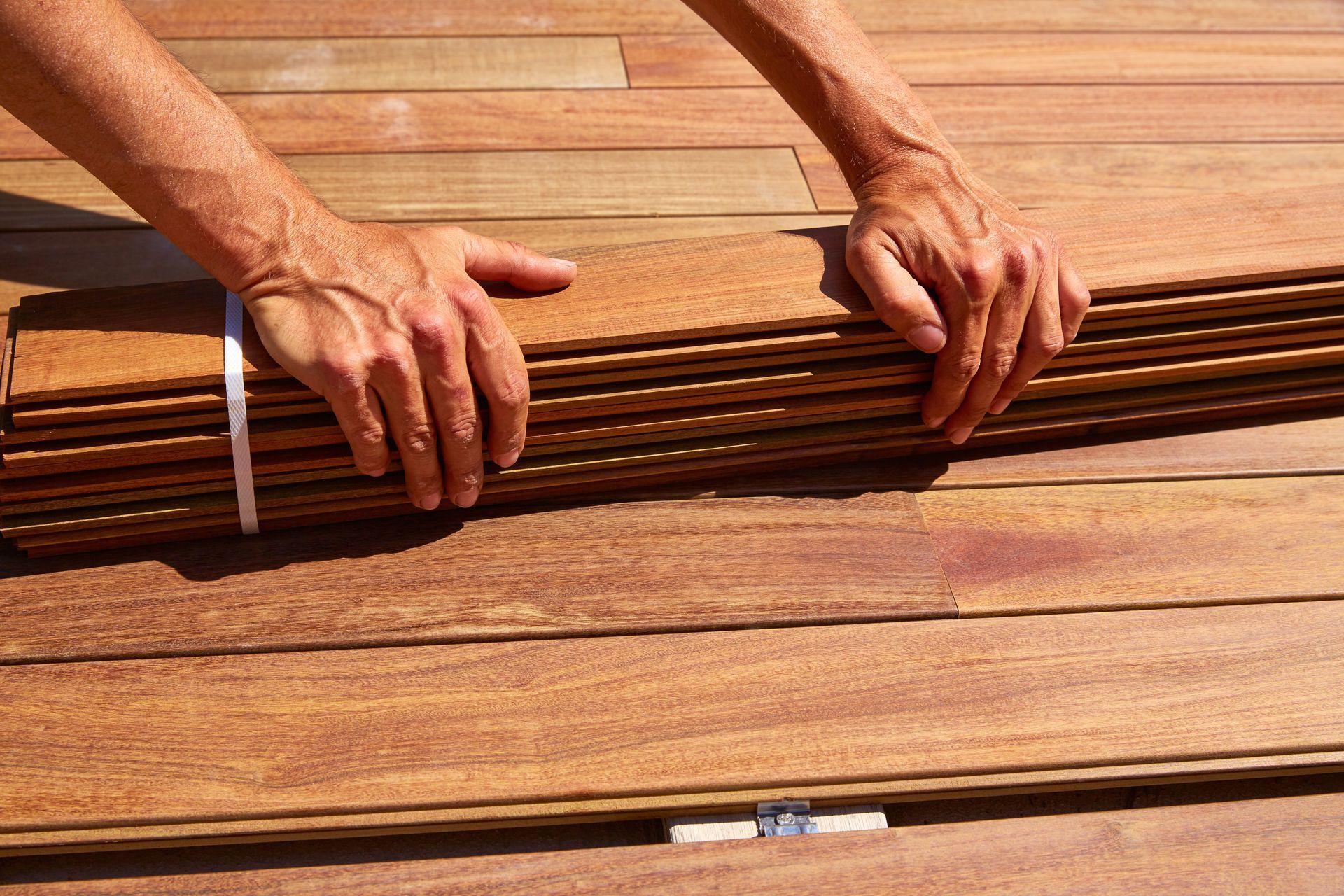 Hands holding a bundle of brown wood planks on a wood surface.