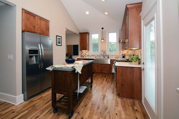 Kitchen with stainless steel refrigerator, wooden cabinets, island, and wood floor.