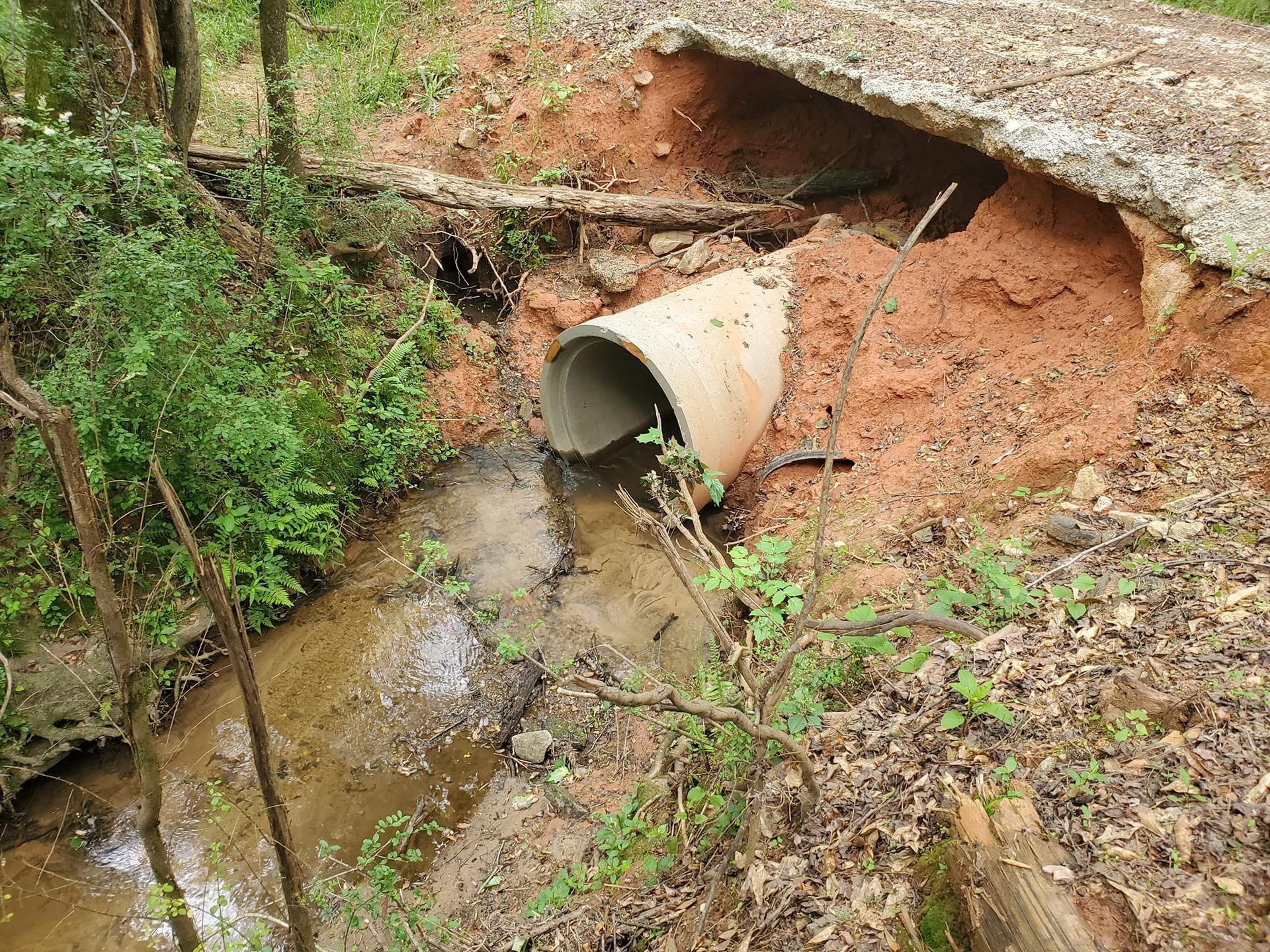 Culvert pipe draining muddy water into a small creek beside an eroded dirt bank