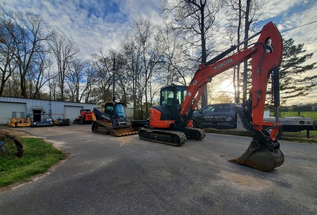 Three excavators parked on a paved lot beside a building under a cloudy sky.
