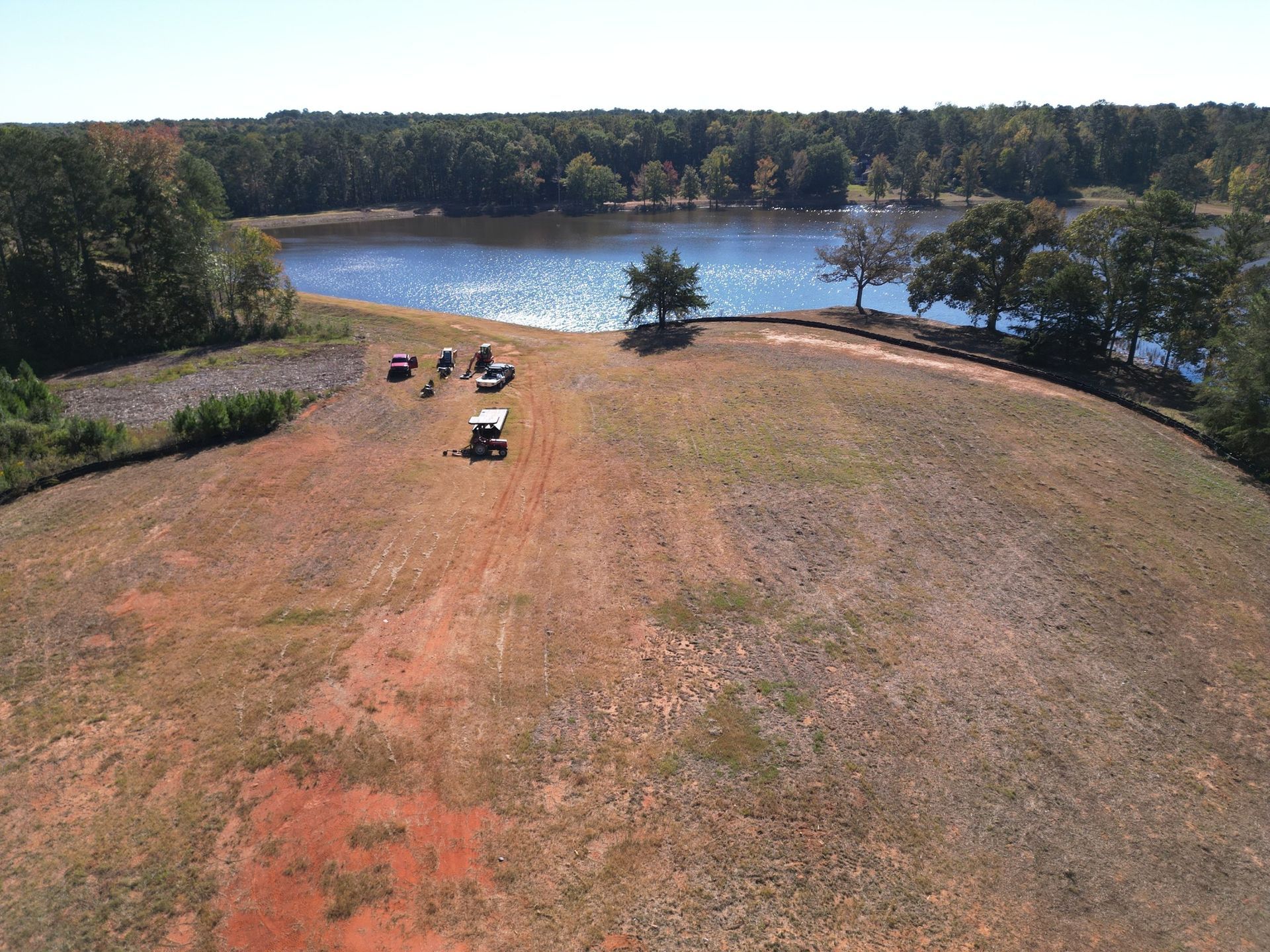 Grassy lakeside field with parked vehicles and trees under a clear sky