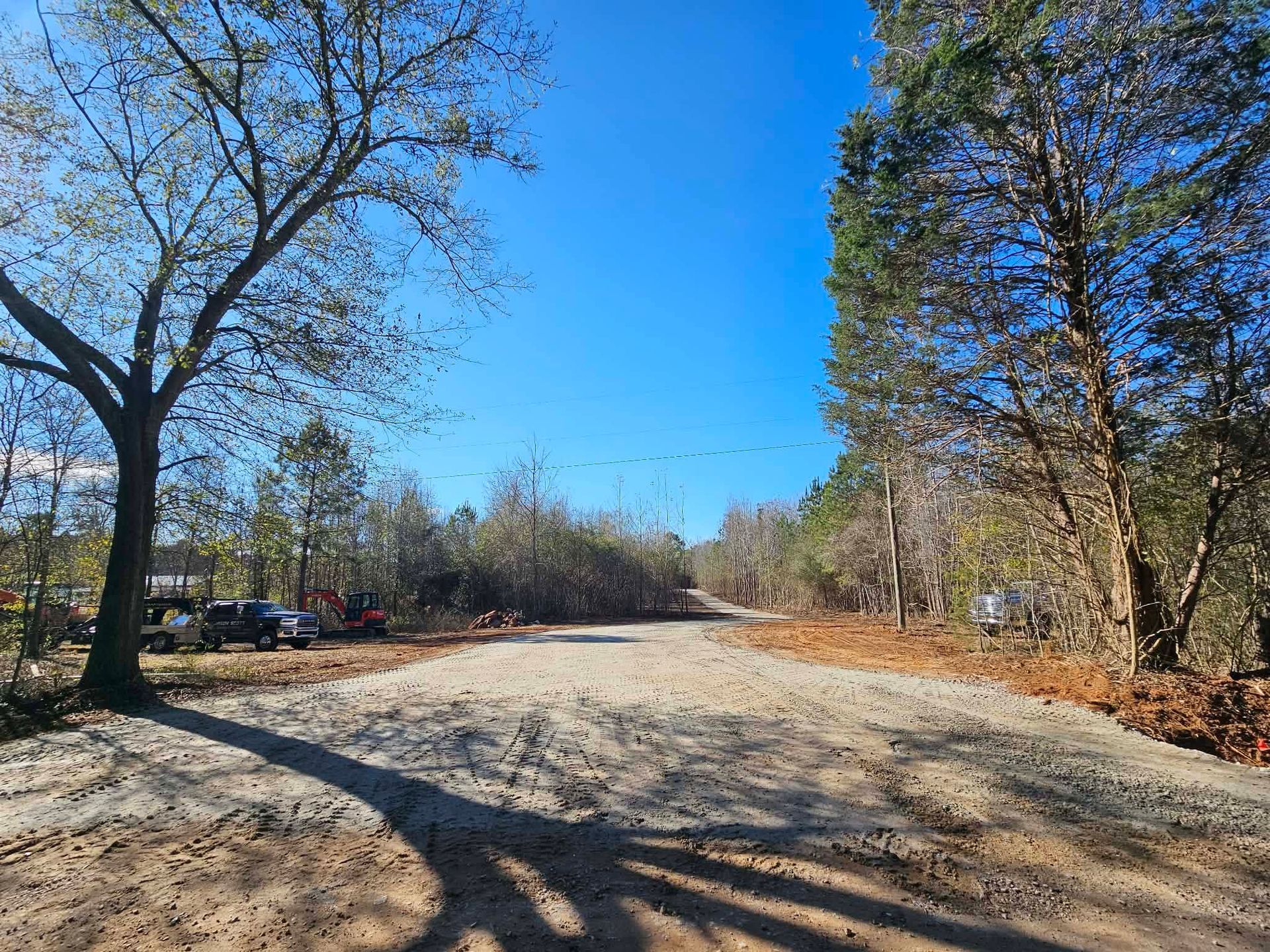 Wide gravel road with trees and parked cars under a clear blue sky