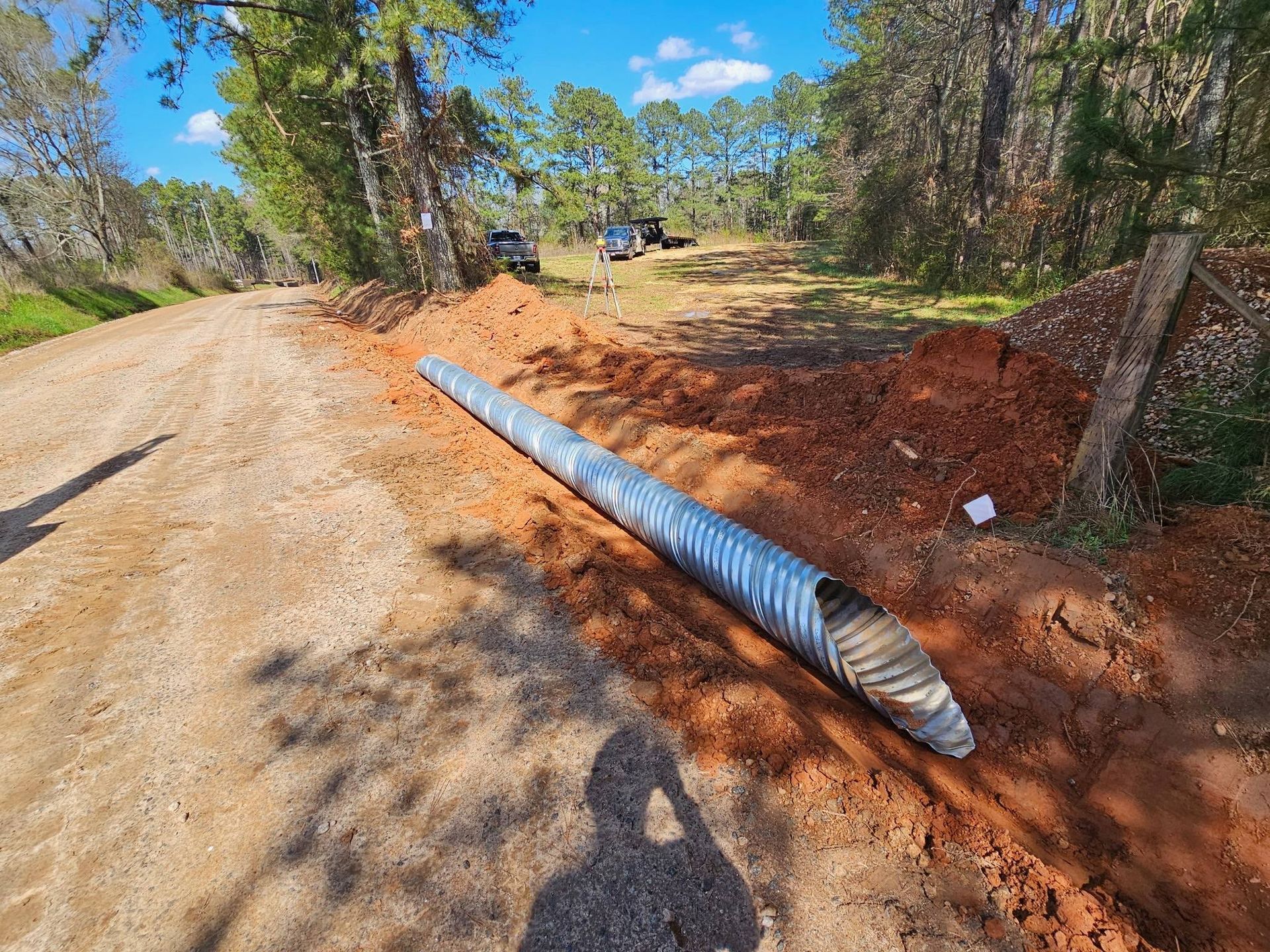 Blue corrugated pipe beside a dirt road and red soil embankment in a wooded area