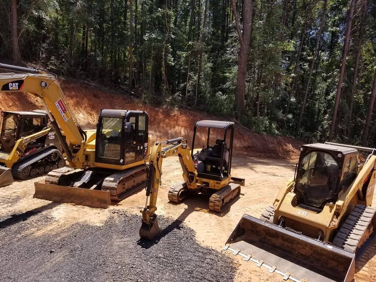Three excavators on a dirt site in a wooded area