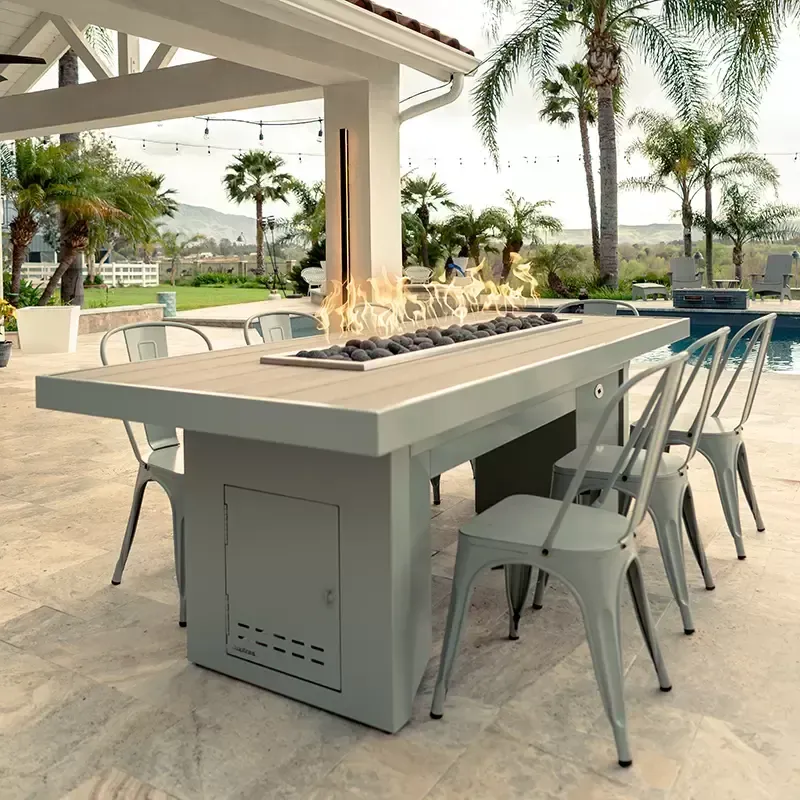 Modern outdoor patio with a long fire pit dining table and metal chairs under a covered terrace.