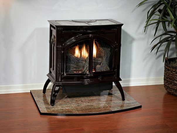Small black electric fireplace stove glowing on a rug in a room with hardwood floors and a plant.