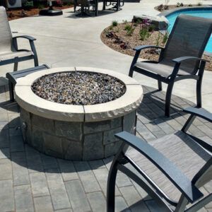 Outdoor patio with a stone fire pit surrounded by black metal chairs on a paved patio