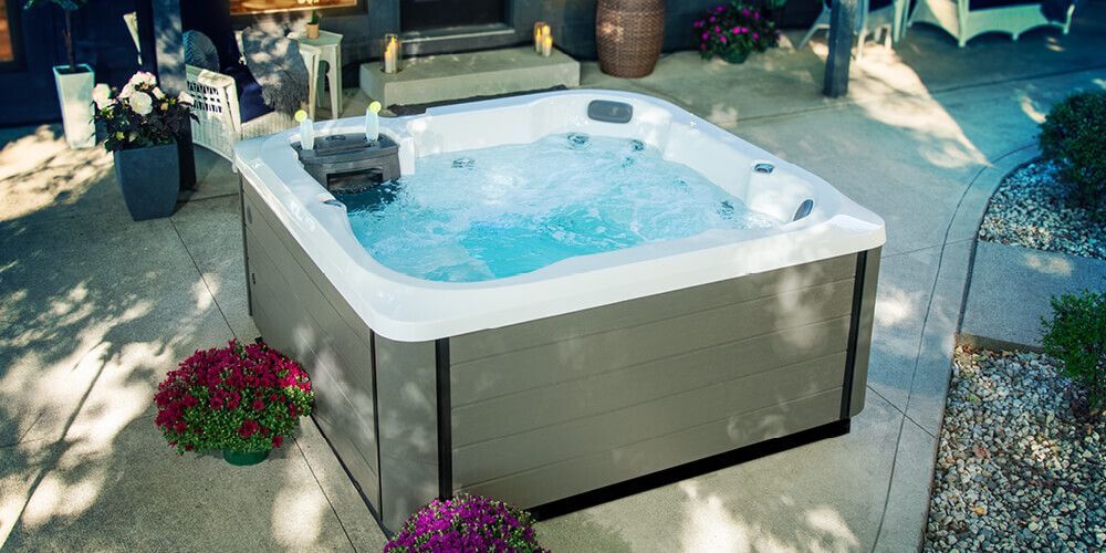 Outdoor hot tub bubbling on a patio, with potted plants and gravel landscaping.