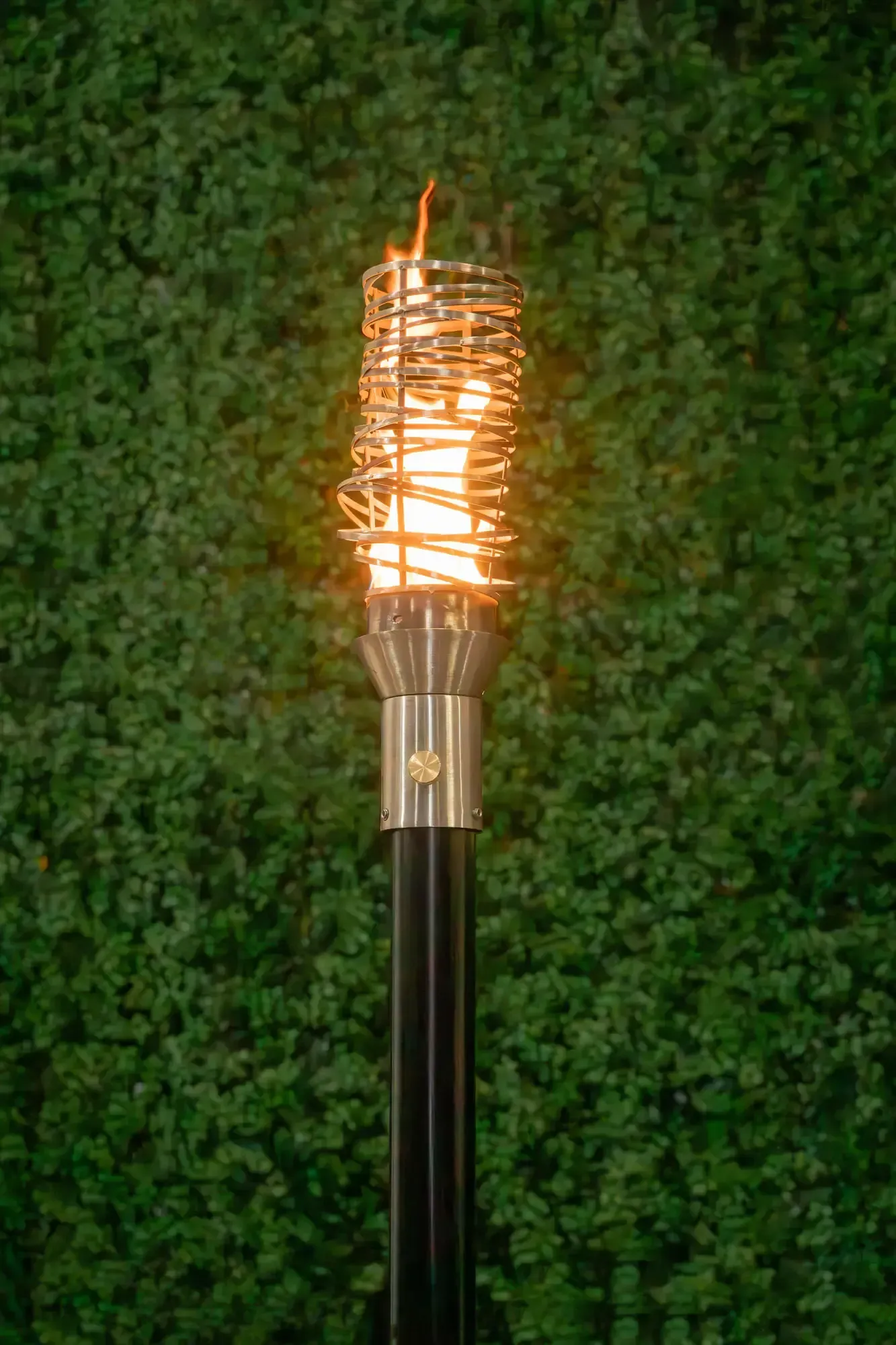 Lit tiki torch with a bright flame against a green hedge background