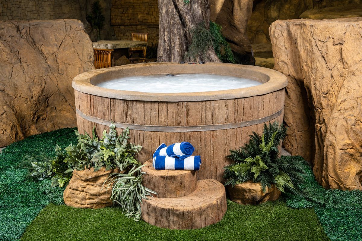 Wooden outdoor spa tub with blue-and-white towels on a small step, surrounded by plants and greenery