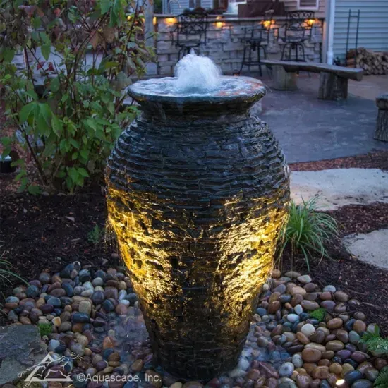 Illuminated stone water fountain bubbling in a landscaped courtyard at dusk