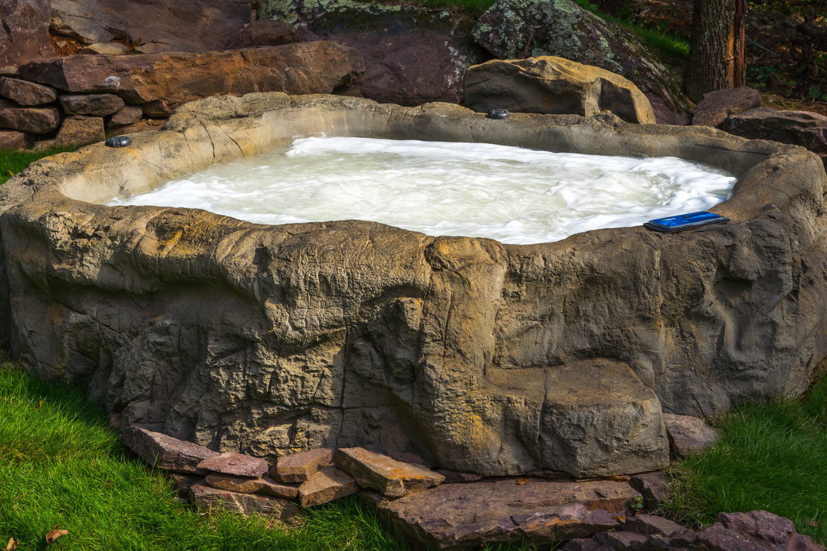 White mineral pool in a rocky stone basin with green grass around it.