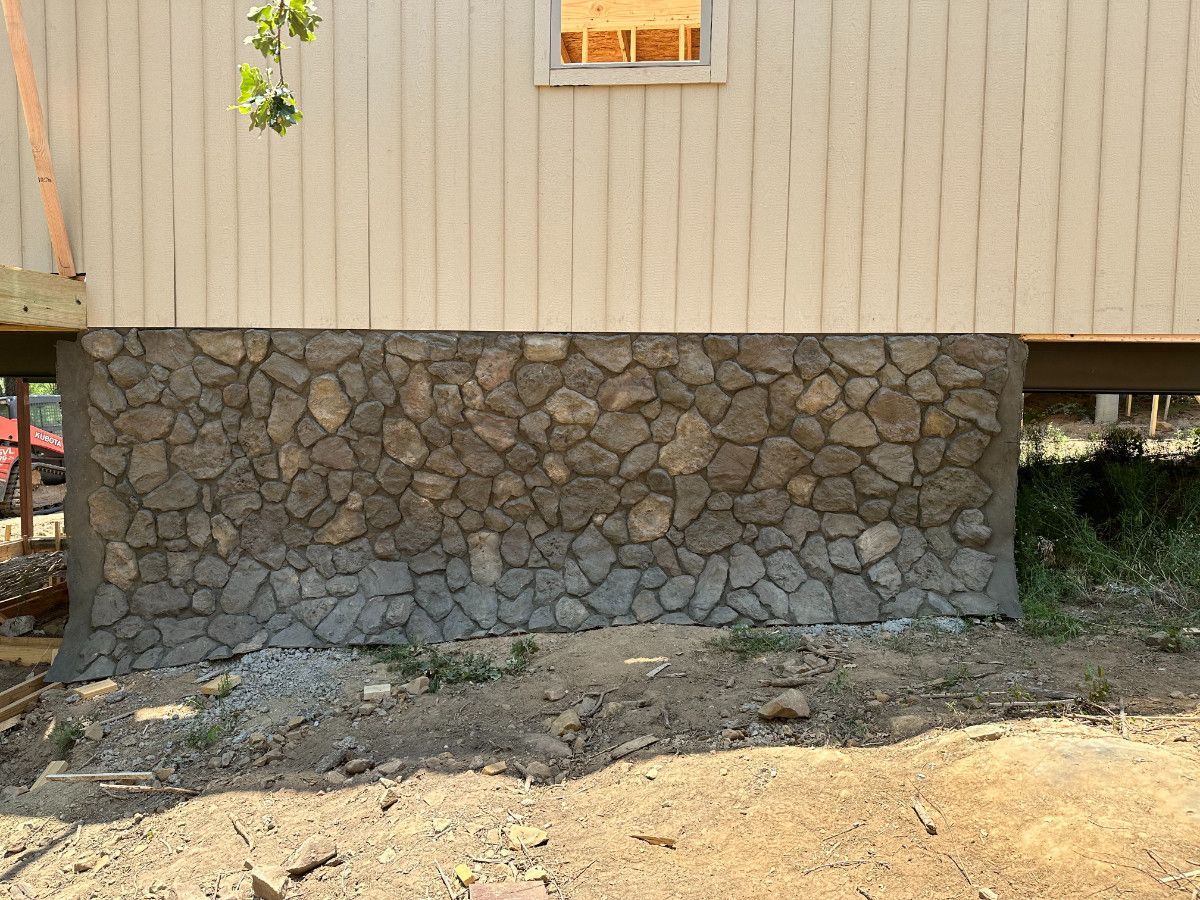 House exterior with tan siding and stone foundation above a dirt yard
