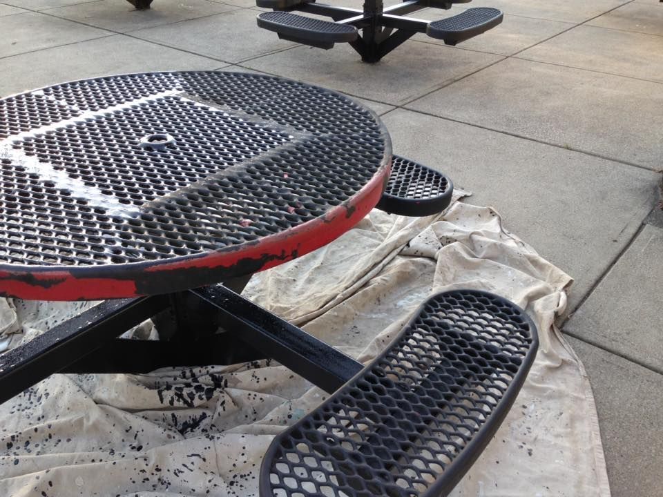 A round metal picnic table with a red rim sits on the sidewalk