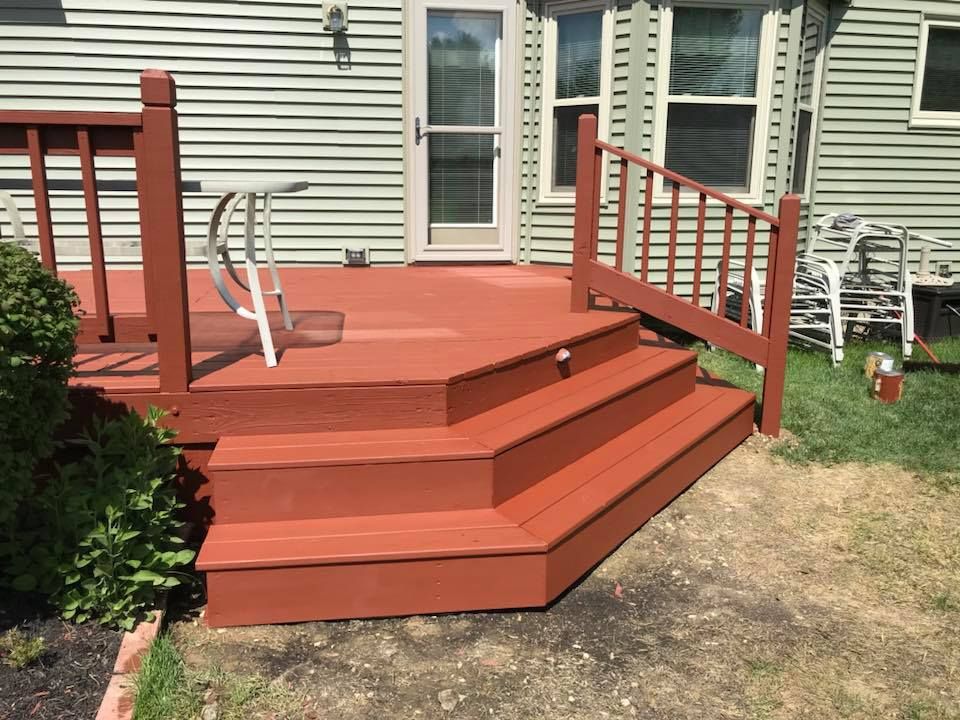 A red deck with stairs and a railing is in front of a house.