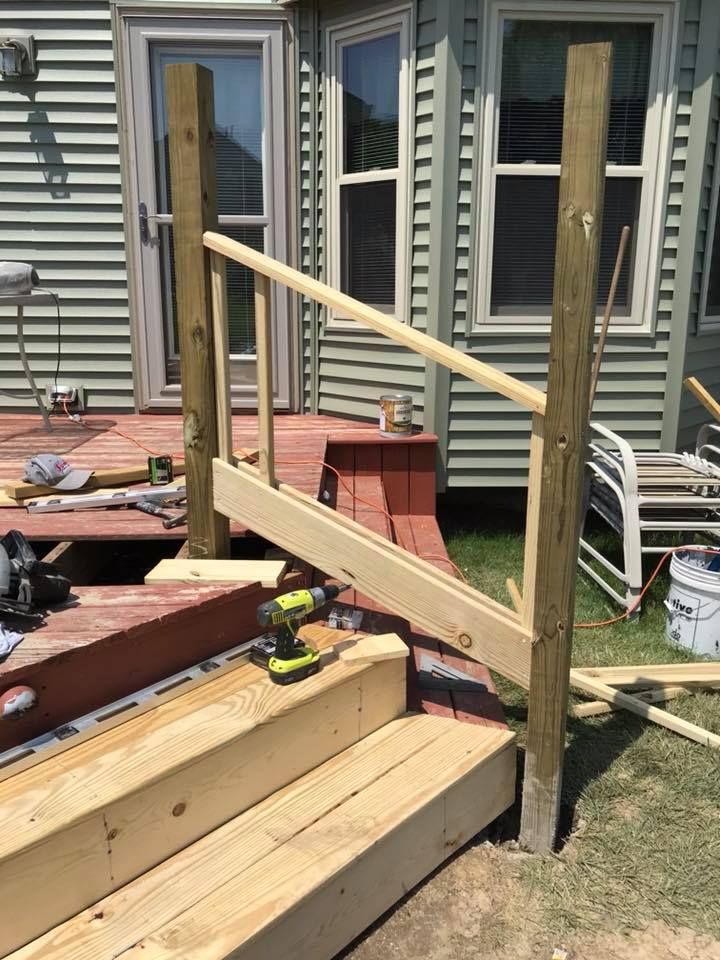 A wooden railing is being built on a deck in front of a house.