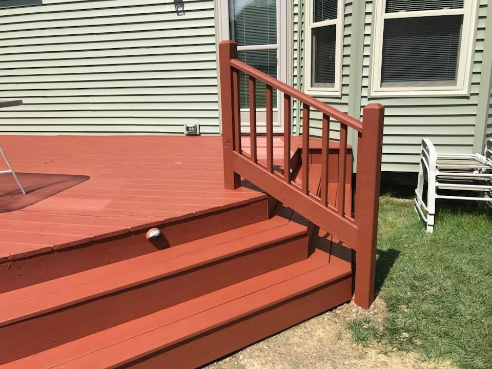 A red deck with stairs and a railing in front of a house.