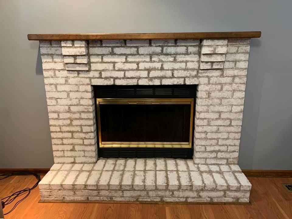 A white brick fireplace with a wooden mantle in a living room.