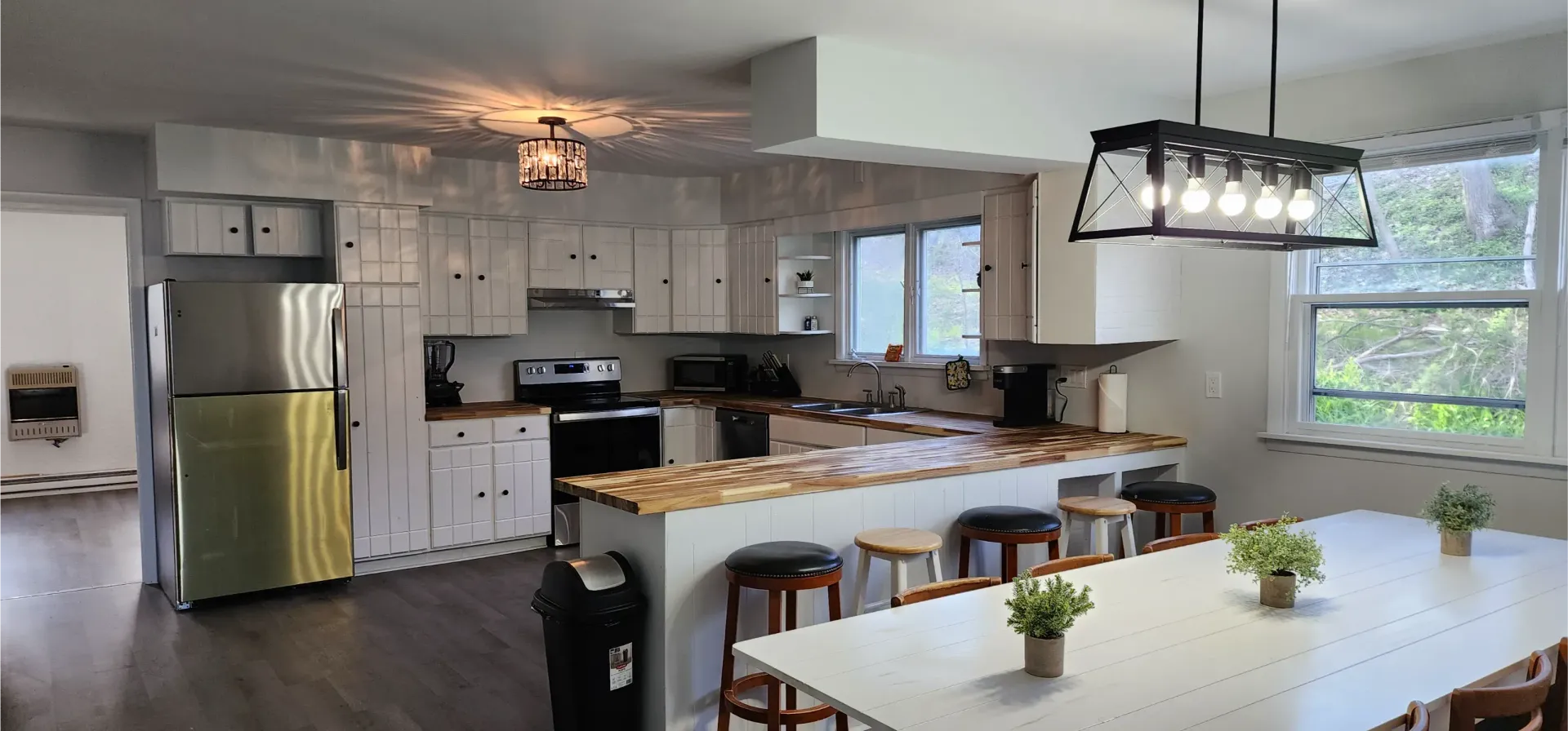 Bright kitchen with white cabinets, wood countertops, stainless steel appliances, and a large dining table with stools.