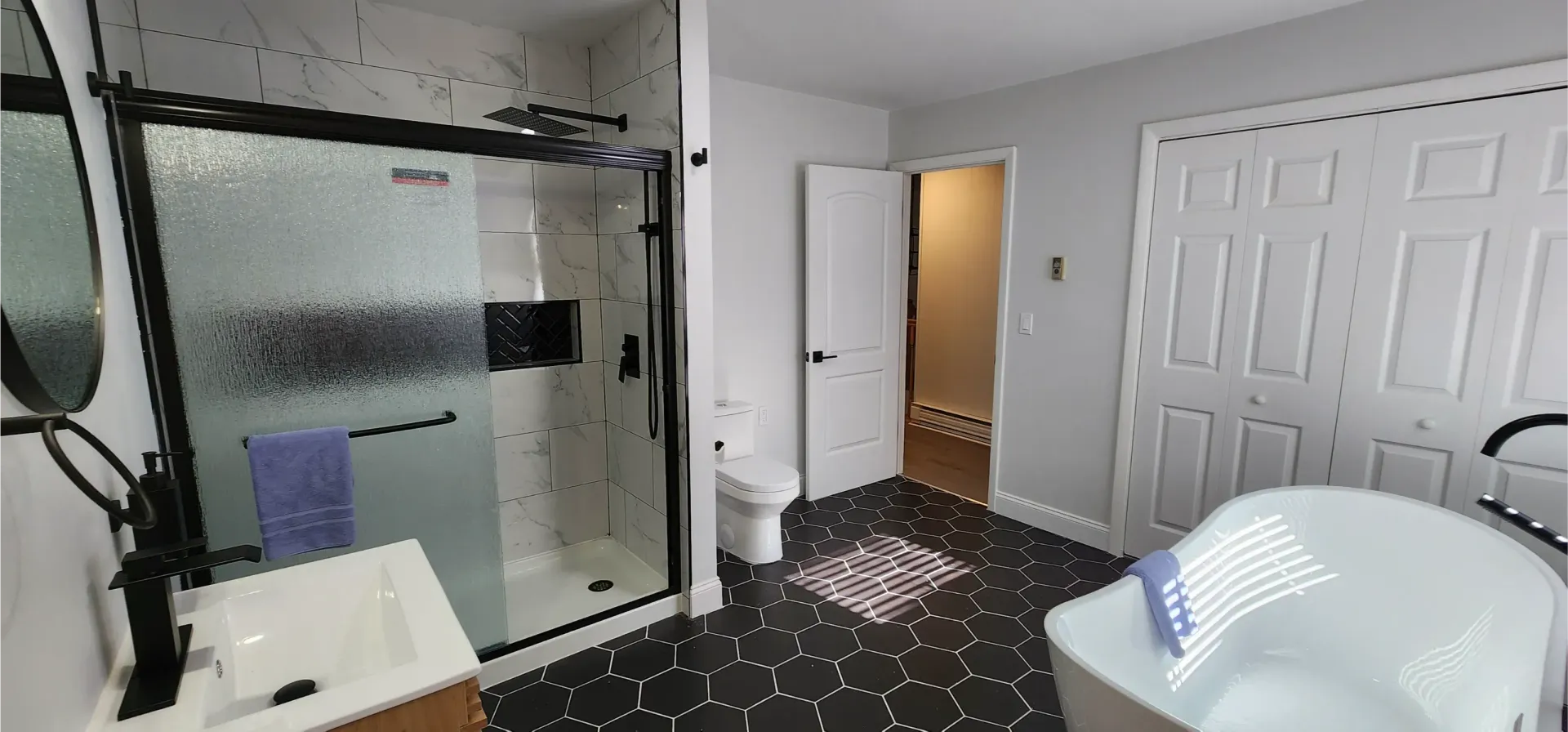 A modern bathroom with a glass-enclosed shower, a white soaking tub, and black patterned flooring.