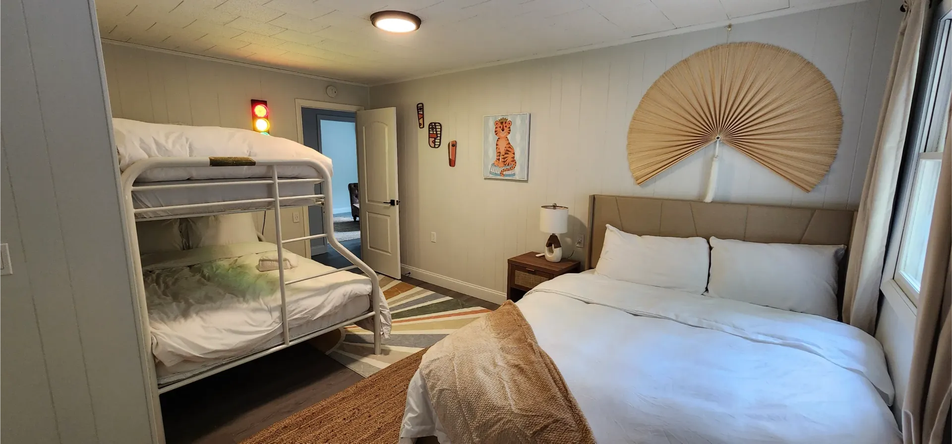 A hotel bedroom featuring a bunk bed on the left, a queen bed with white bedding, and a large fan wall decoration.