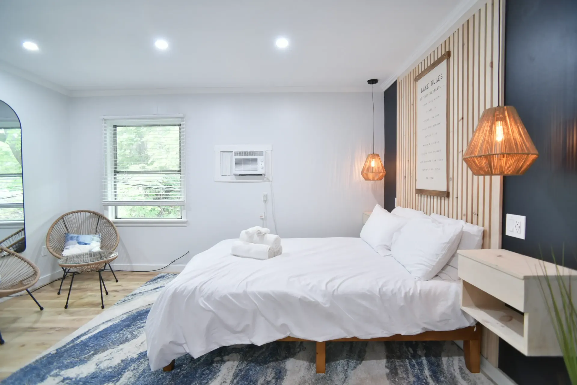 A cozy bedroom with a platform bed, white bedding, natural wood accent wall, hanging pendant lights, and a blue rug.