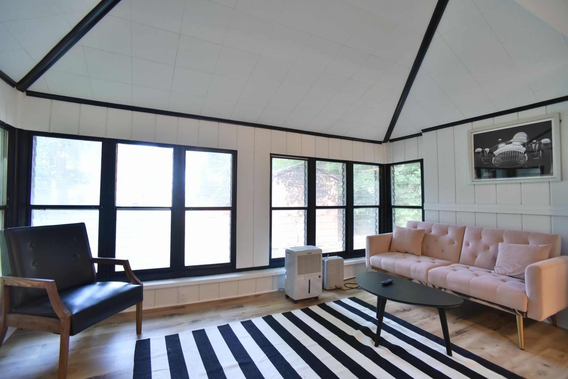 A modern living room with black-trimmed windows, a light pink sofa, a black leather armchair, and a striped area rug.