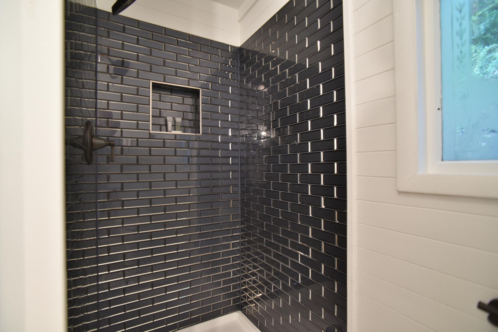 Modern walk-in shower with glossy black subway tiles, a recessed niche, black fixtures, and white shiplap walls.