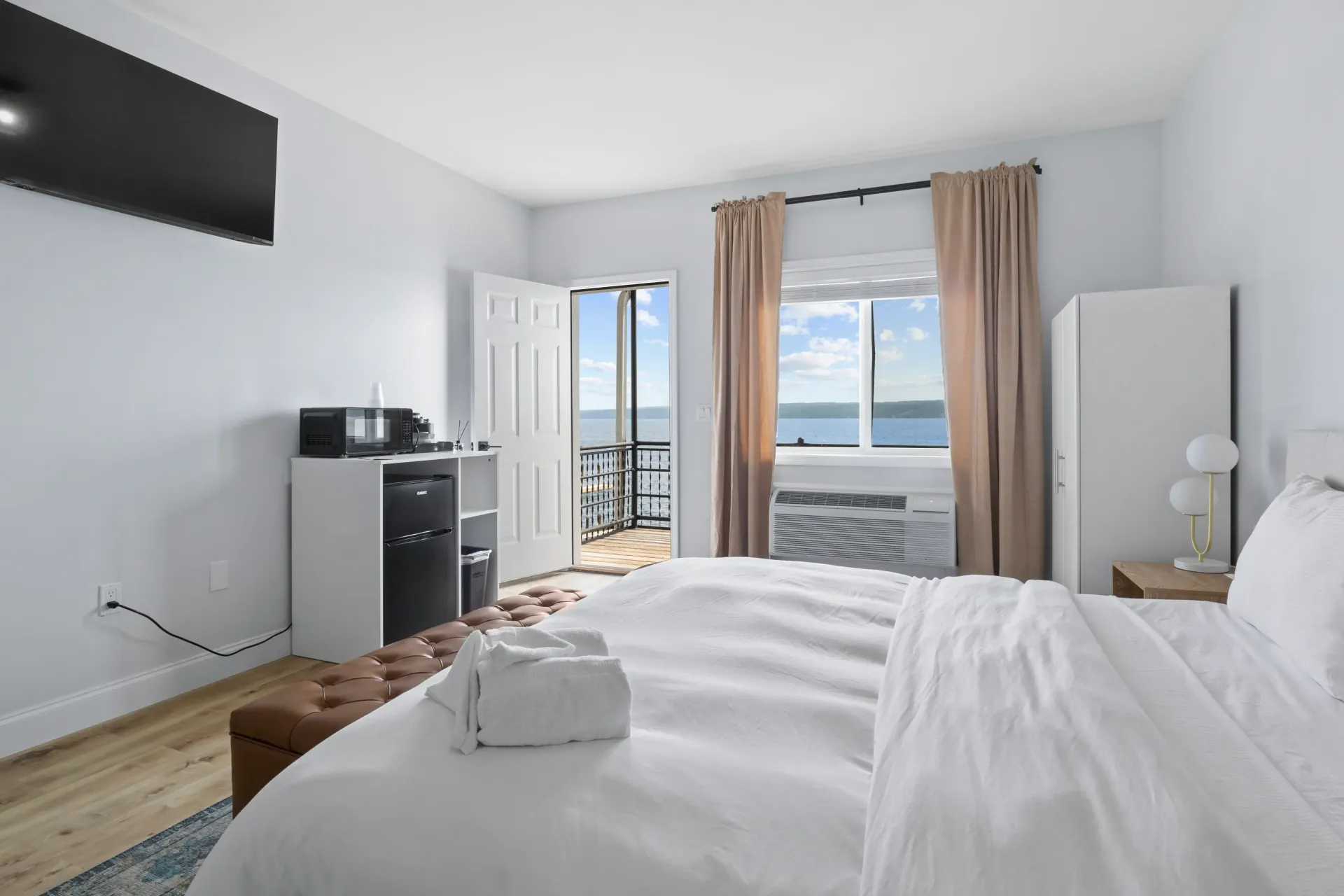 A hotel room with a large bed, a white cabinet, and an open door leading to a balcony with an ocean view.