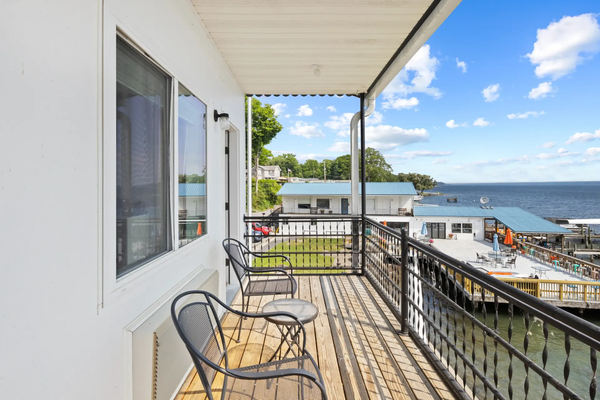 A balcony with chairs overlooking a body of water under a blue, cloudy sky.