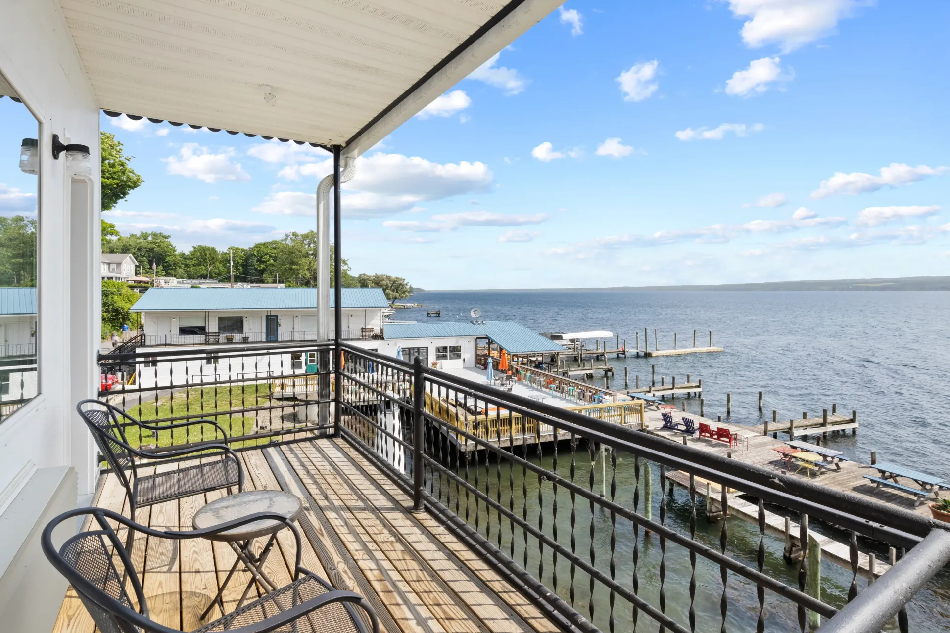 A balcony with metal chairs overlooking a wooden pier, docks, and a lake under a clear blue sky.