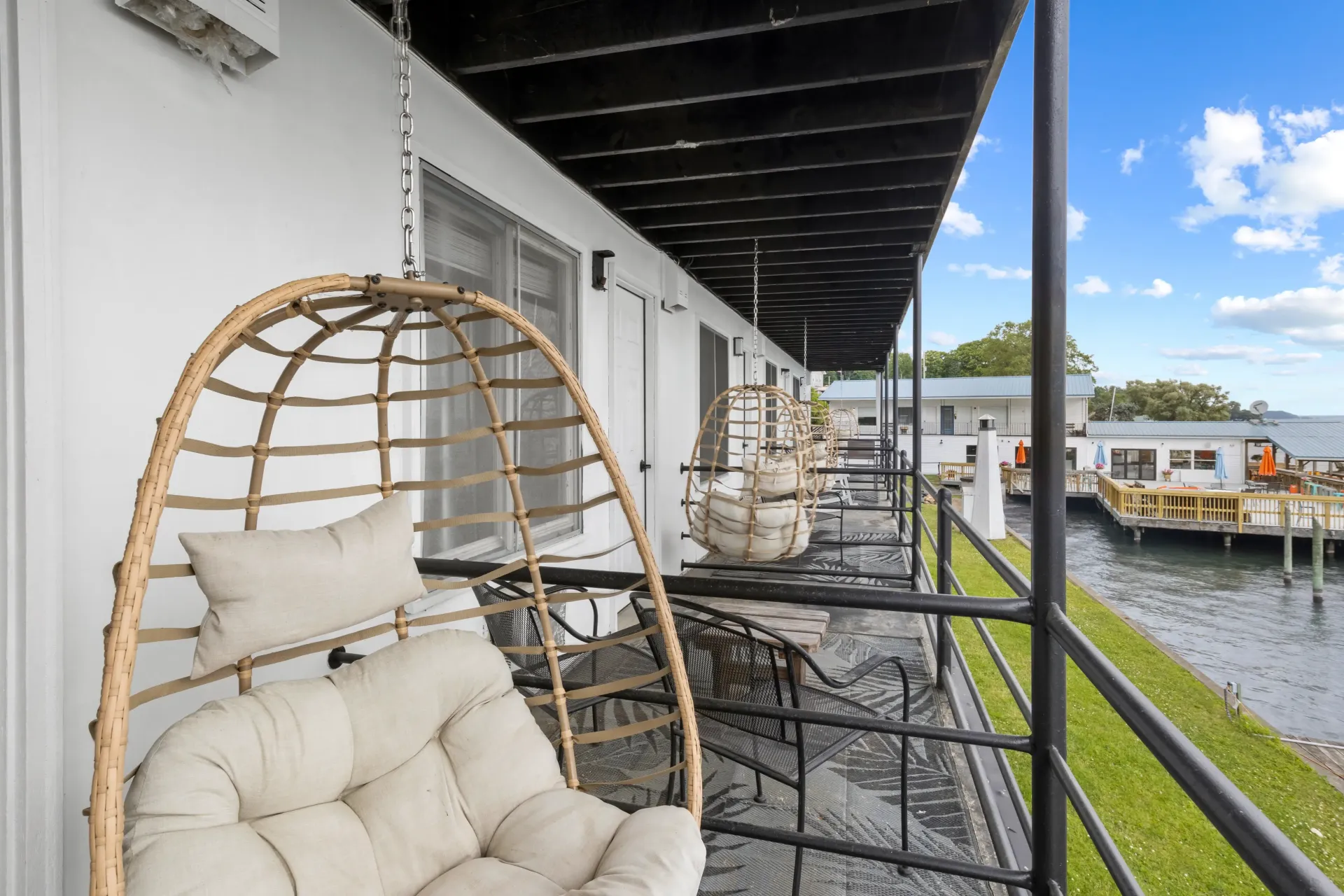 A row of wicker hanging chairs on a covered balcony overlooking a waterway and floating docks.