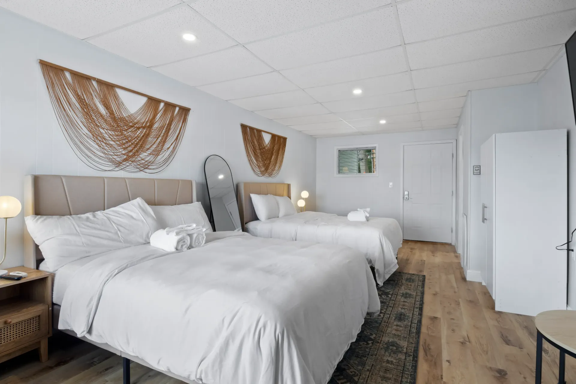 A hotel room featuring two queen-size beds with white linens, beige headboards, and decorative wall art on light walls.