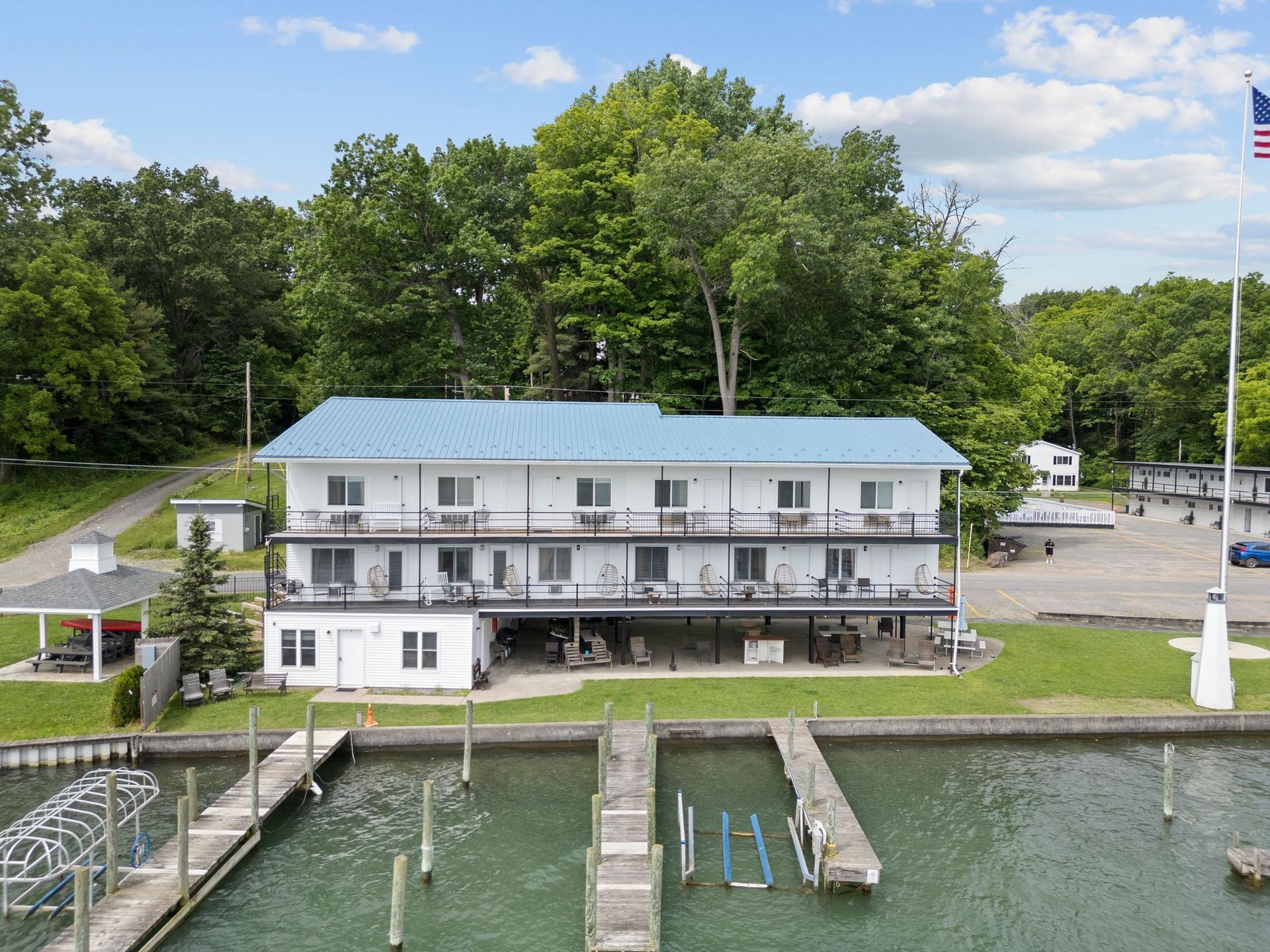 A two-story white waterfront hotel with a blue metal roof, featuring balconies overlooking a dock on a sunny day.