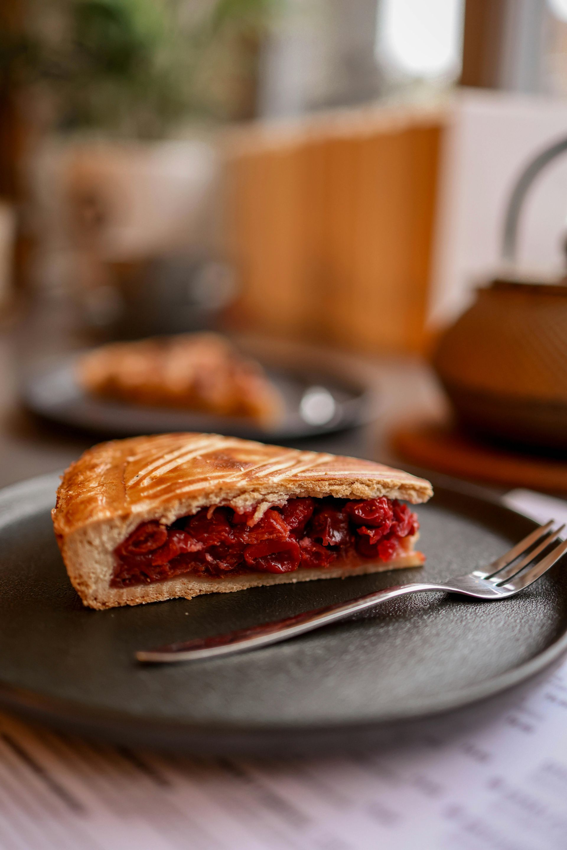 Slice of berry pie on a gray plate with a fork on a table, in a softly blurred kitchen setting