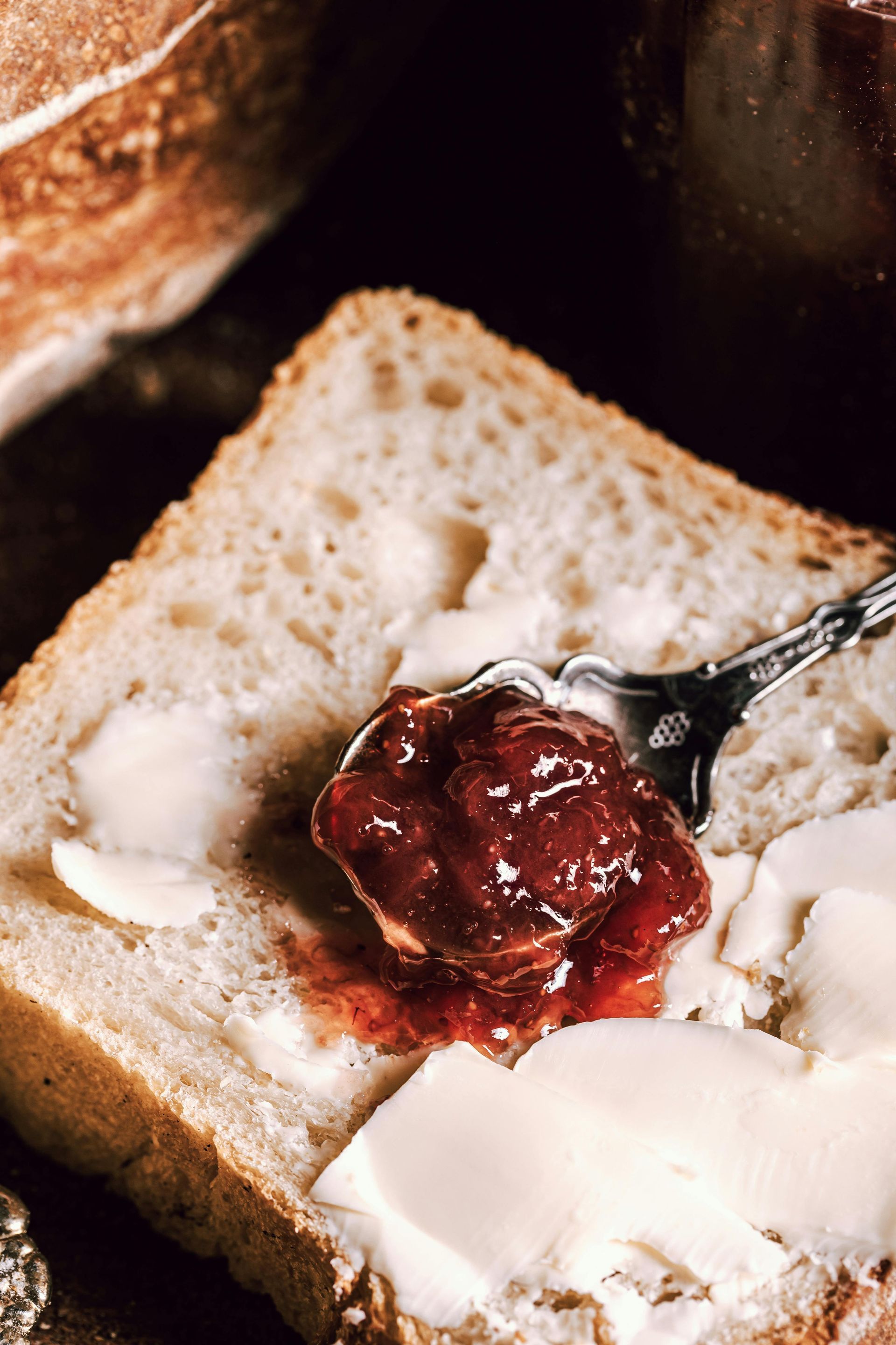 Jam and butter on a slice of white bread, with a spoon in a close-up breakfast scene