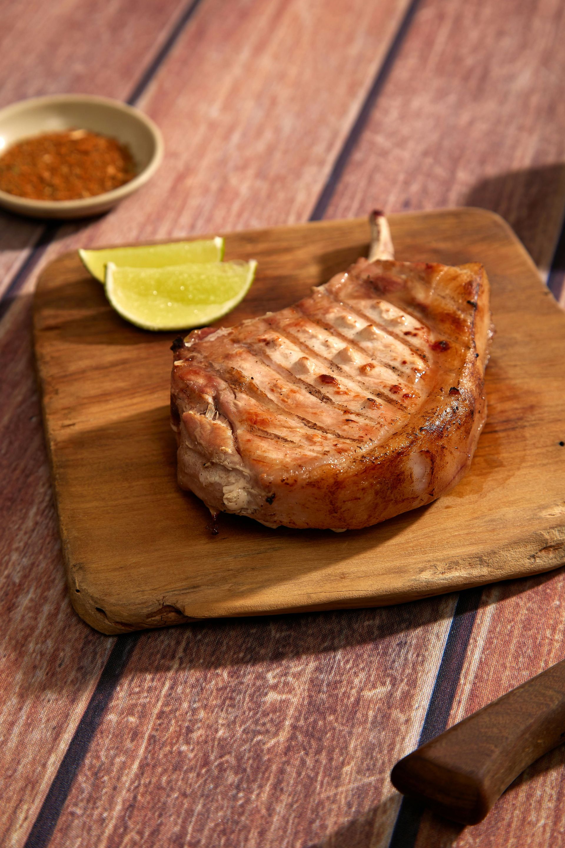 Grilled steak on a wooden board with lime wedges and sauce on a rustic table
