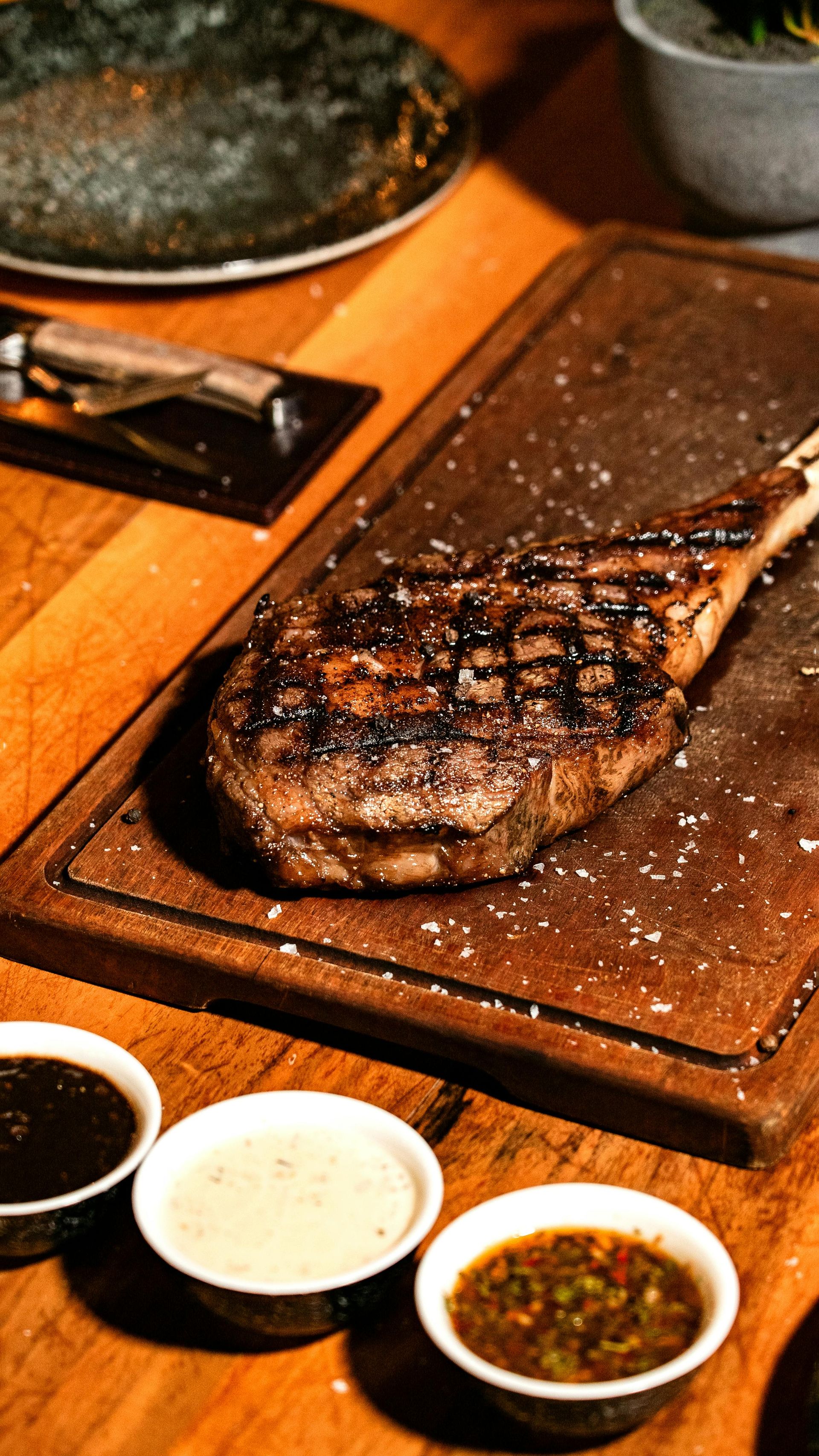 Grilled steak on a wooden plate with dipping sauces on a table