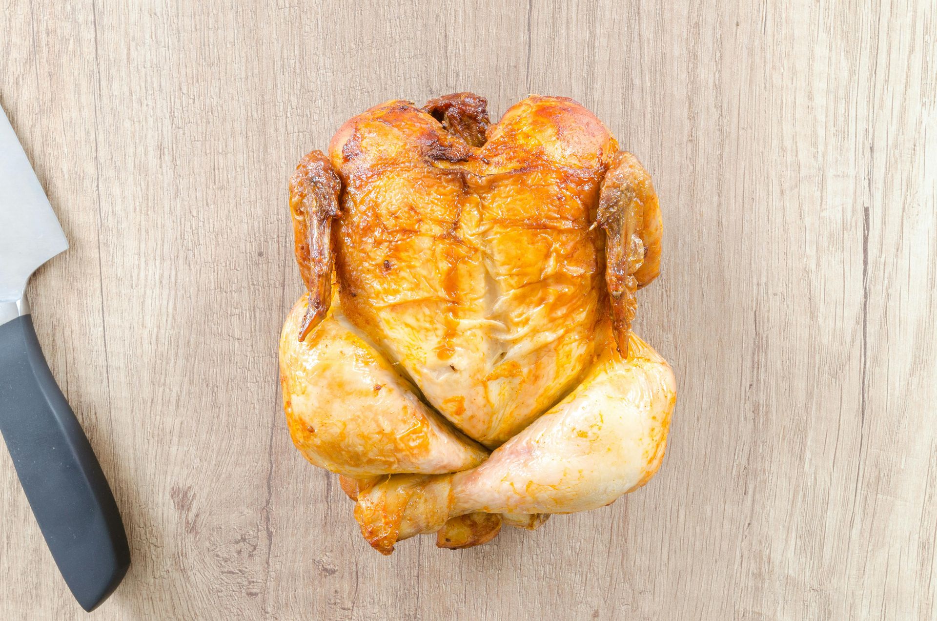 Roasted whole chicken on a wooden cutting board with a knife beside it