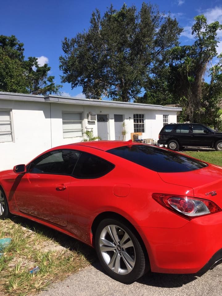 A red car is parked in front of a white house