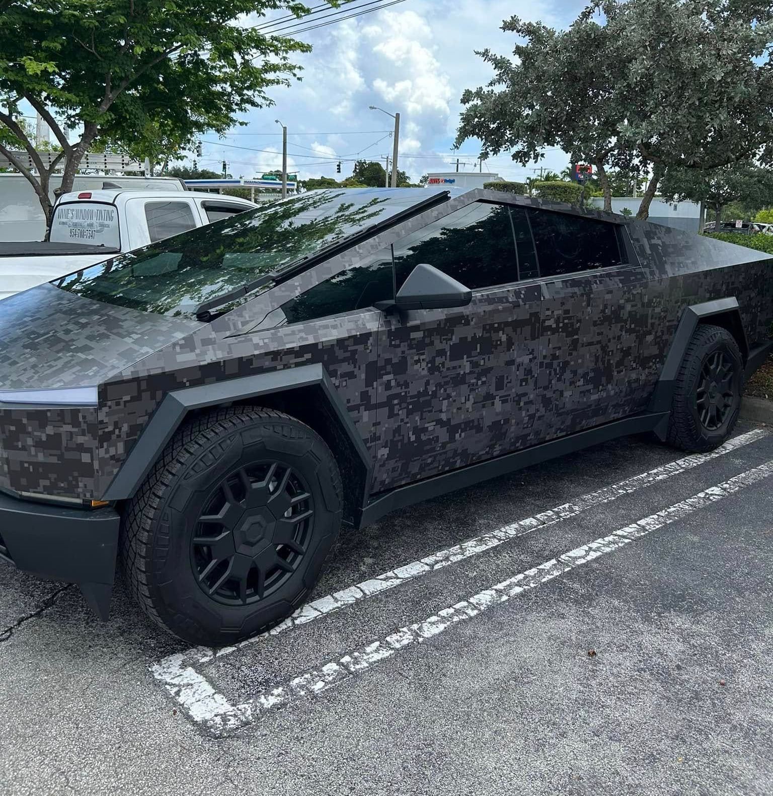 A black car is parked in a parking lot with trees in the background.
