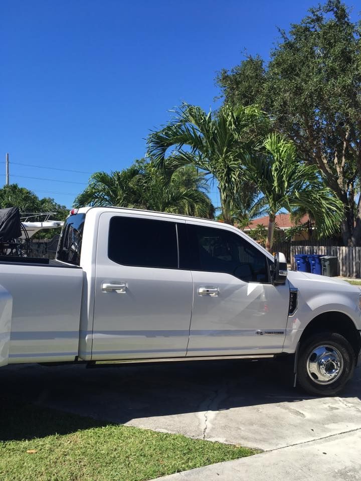 A white truck is parked in a driveway with trees in the background.