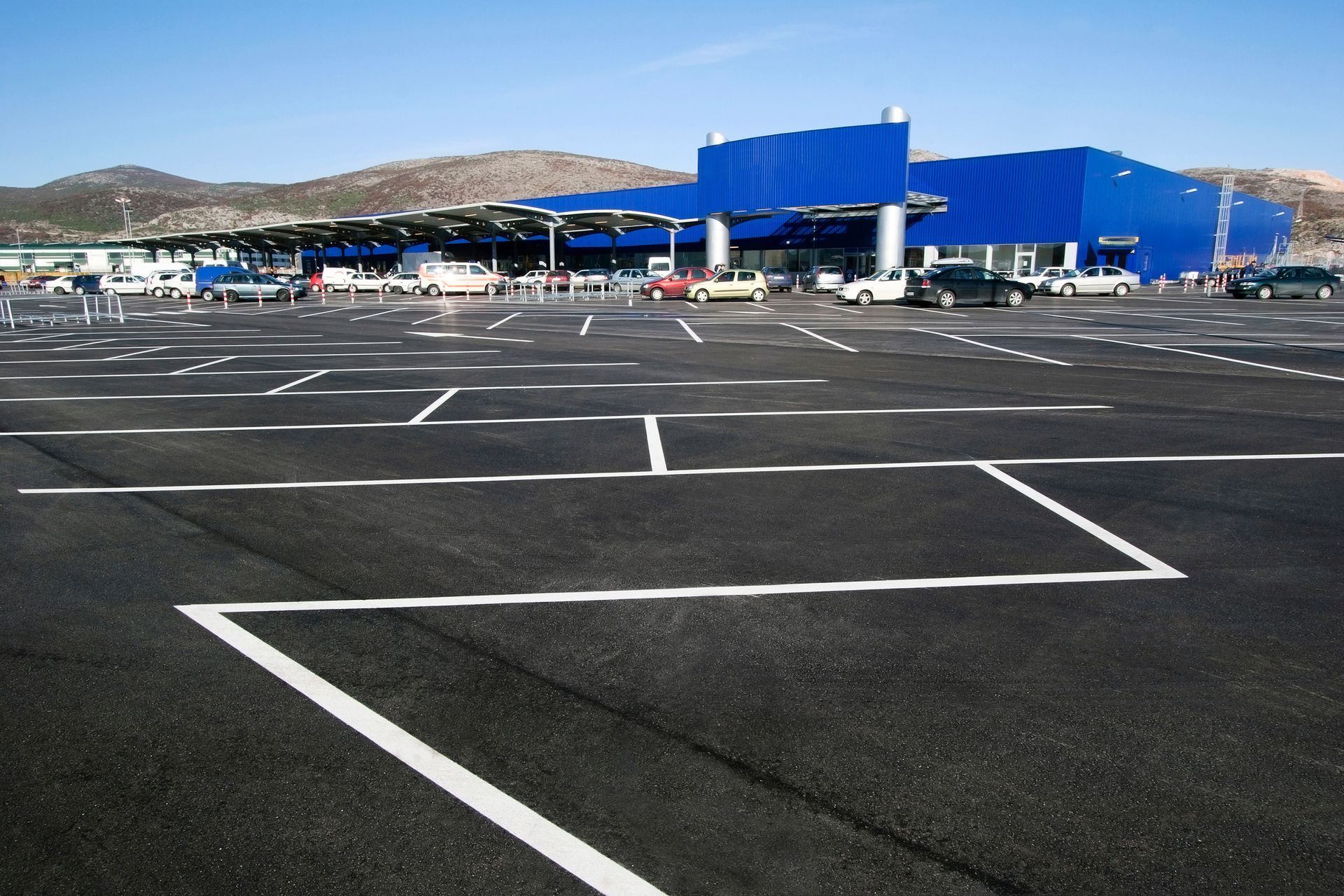Empty parking lot with white markings in front of a blue building and distant hills