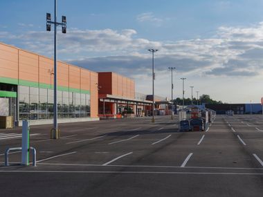 Empty shopping mall parking lot with storefronts and a few carts under a cloudy sky Empty shopping mall parking lot with storefronts and a few carts under a cloudy sky