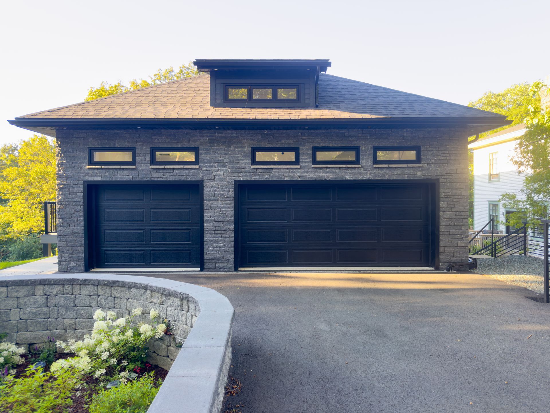 Modern dark-stone house with a three-car garage and curved driveway in bright daylight Modern dark-stone house with a three-car garage and curved driveway in bright daylight
