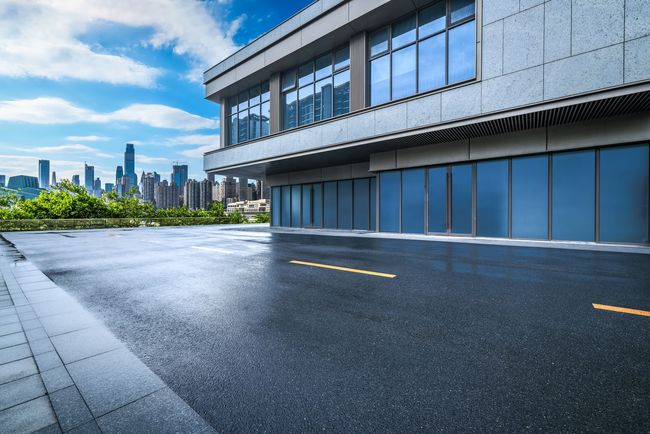 Modern building with reflective windows beside a wet paved road and distant city skyline under a blue sky Modern building with reflective windows beside a wet paved road and distant city skyline under a blue sky