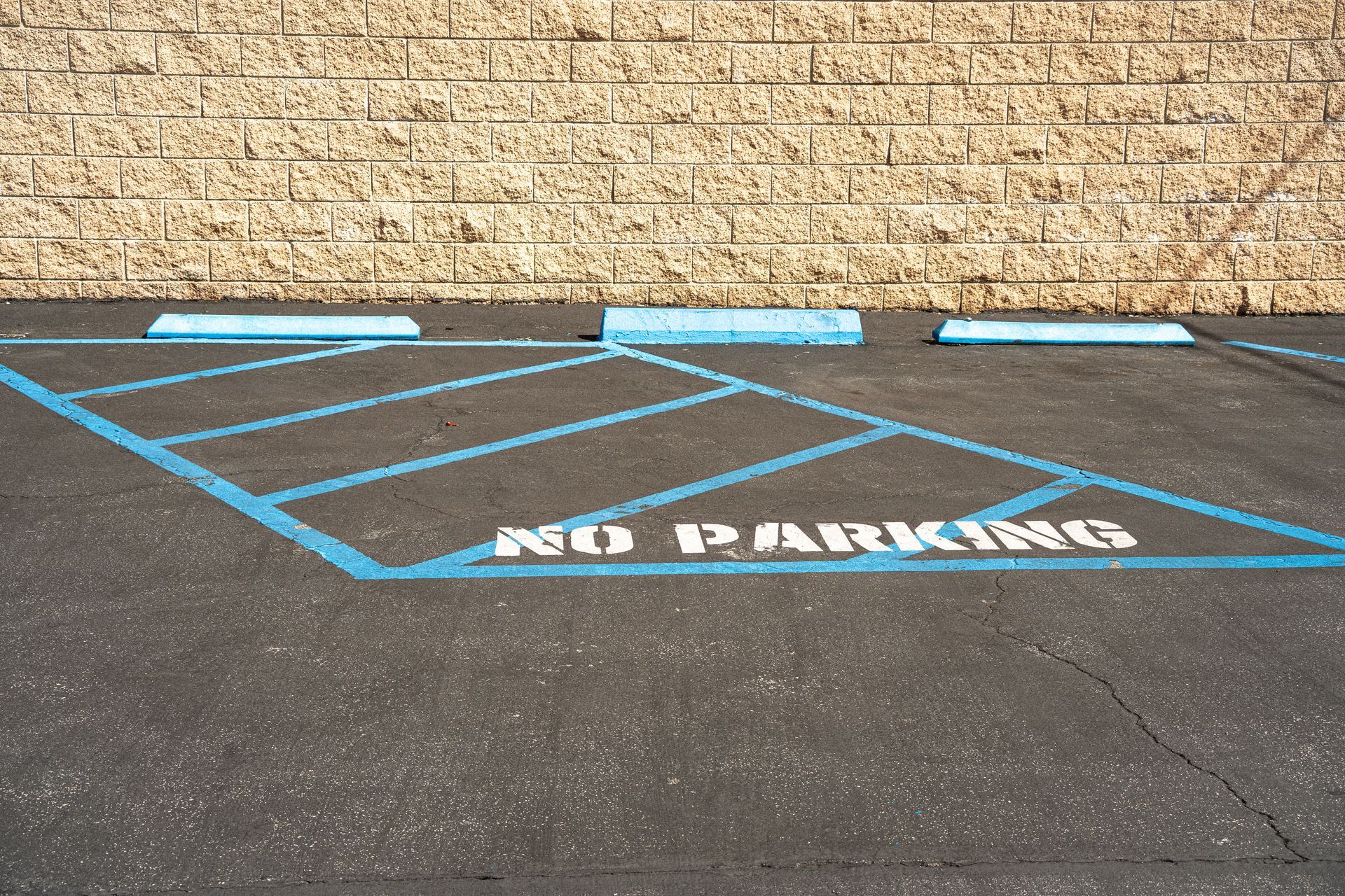 Blue accessible parking space marked “NO PARKING” next to a brick wall. Blue accessible parking space marked “NO PARKING” next to a brick wall.