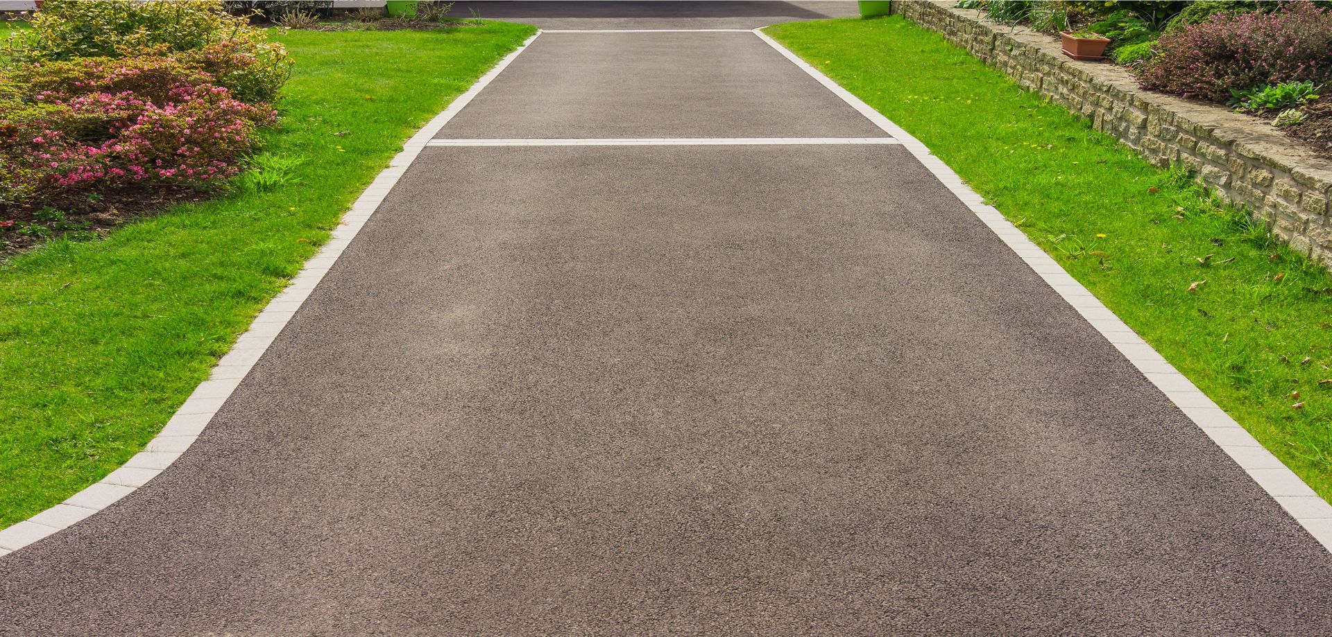 Straight concrete path through a green landscaped garden with flower beds on both sides Straight concrete path through a green landscaped garden with flower beds on both sides