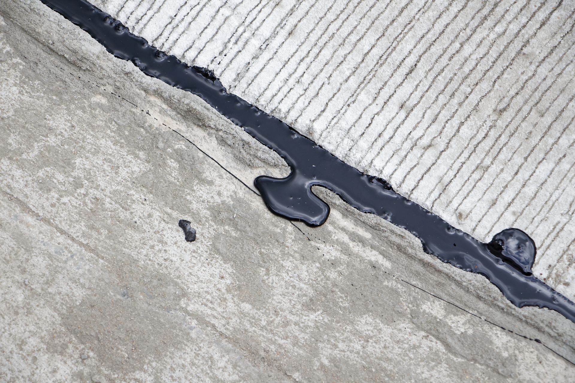 Cracked concrete and corrugated metal roof seam sealed with black caulk
